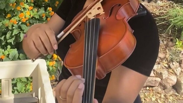 Uma menina violinista da Orquestra Jovem Theatro São Pedro segura o violino com as mãos em posição como se estivesse tocando.